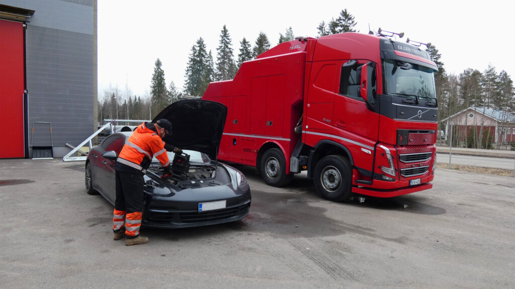 Punainen hinausauto ja hinausalan ammattilainen antamassa tiepalvelua mustalle henkilöautolle