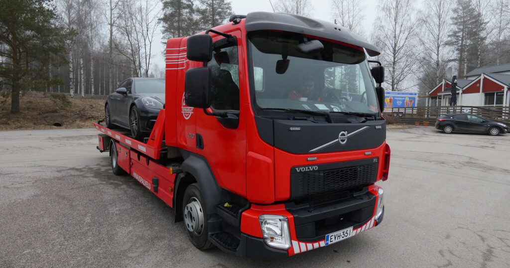 Punainen hinausauto kuljettaa henkilöautoa